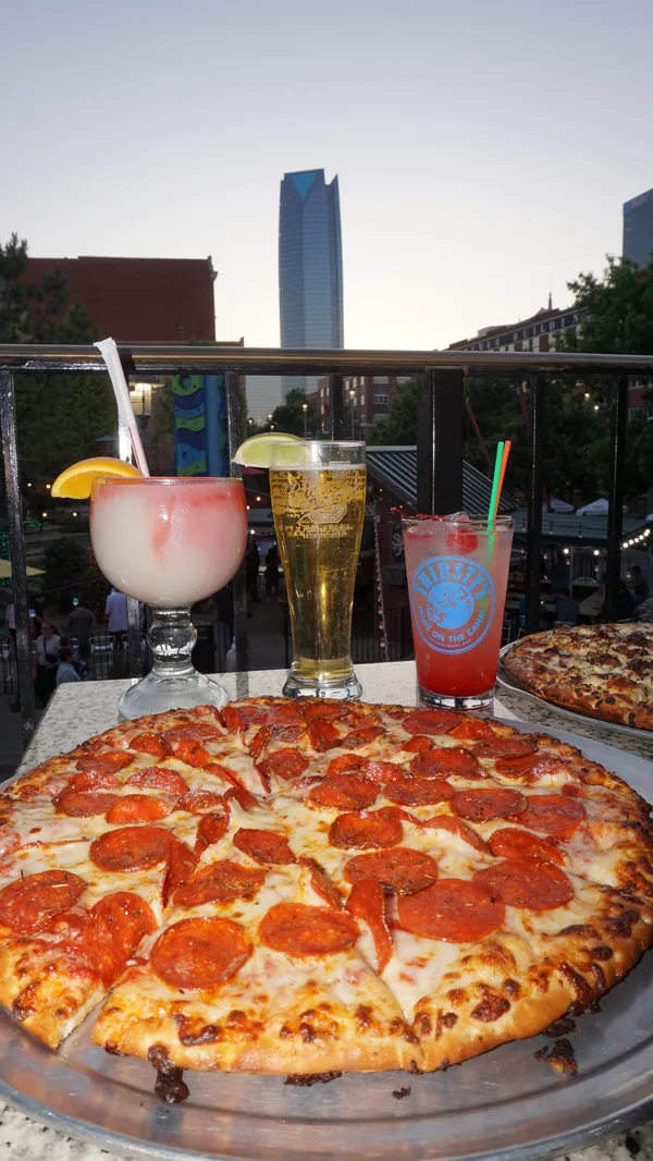 Pizza and cocktails on the Thirsty's patio rail with the Oklahoma City skyline behind at dusk